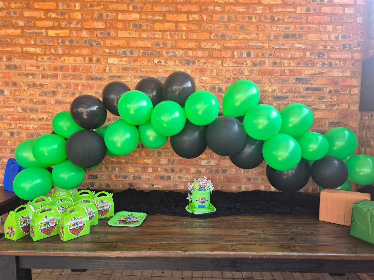 Green and black balloon arch over a kids party table